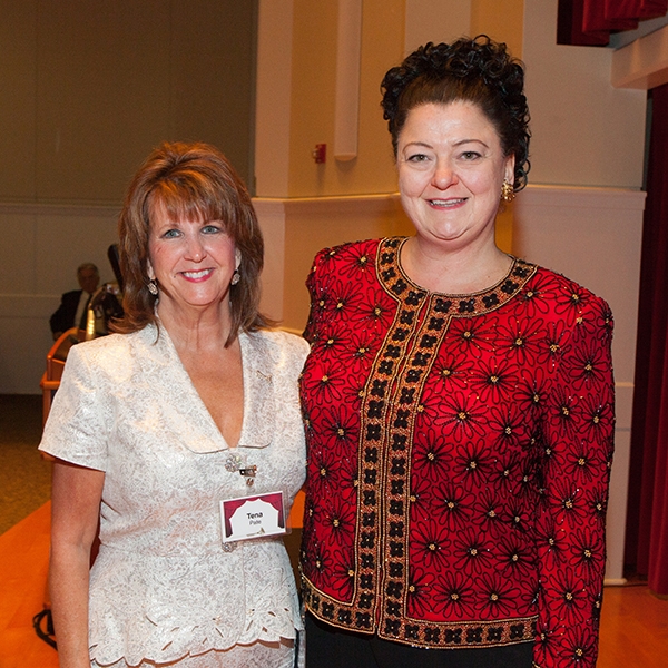 A photo of Tena Pate wearing a white blouse, smiling, standing next to a taller woman in a red blouse