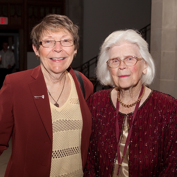 A photo of Kitty Hoffman and another woman, both wearing gold blouses and garnet outerwear