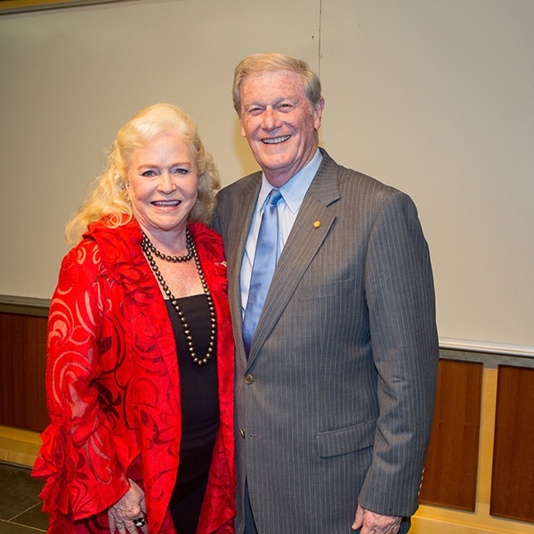 A photo of Sharon Lechter wearing a red jacket, smiling, standing with a man wearing a gray suit