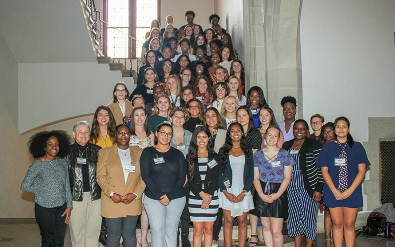 The 2018 Women's Leadership Institute, over fifty women, gathered indoors on stairs, smiling at the camera